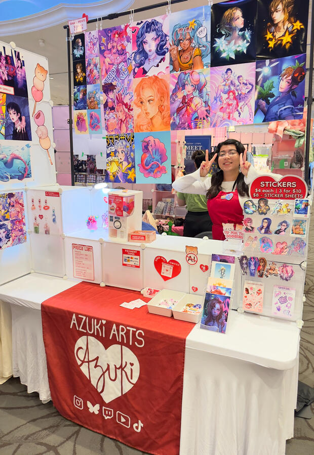 Azuki Arts artist alley vendor booth at Video Game Live Expo (VGLX) 2025 in Mississauga, featuring anime and gaming prints, stickers, keychains, and pins.