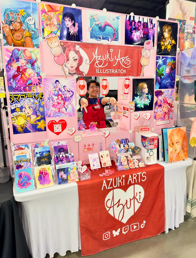 Azuki Arts artist alley vendor booth at Anime Fiesta 2025 in Mississauga, featuring anime and gaming prints, stickers, keychains, and pins.