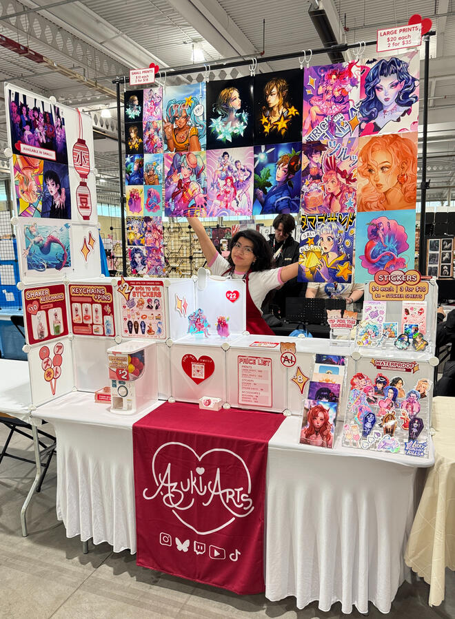 Azuki Arts artist alley vendor booth at Toronto Game Expo 2025, featuring anime and gaming prints, stickers, keychains, and pins.